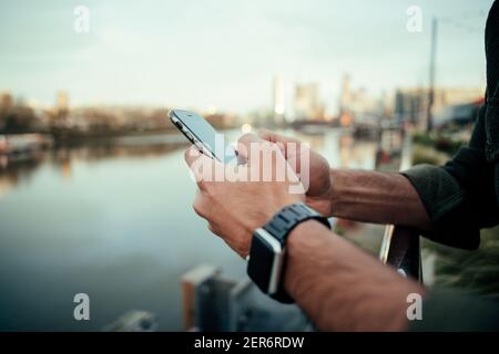 Close up mixed race male typing on smartphone while walking along harbour enjoying the outdoors Stock Photo