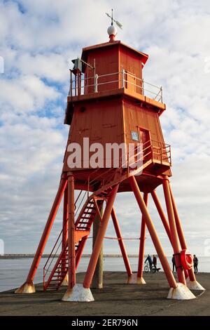 The bright red painted Herd Groyne Lighhouse stands in the mouth of the River Tyne at Littlehaven, South Shields in Tyne and Wear.