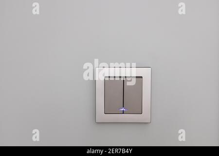 Fashionable modern silver light switches on a gray wall, opposite view. Switch with night illumination. Concept interior details, electrical equipment Stock Photo