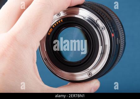 hand holding modern digital 50 mm dslr lens on blue background - close-up with selective focus. Stock Photo