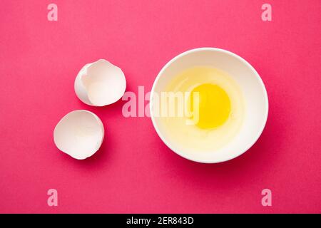 Broken egg in bowl near shell on pink surface Stock Photo
