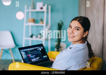 Portrait of young woman mobile developer with laptop, writes program code on a computer, programmer work. Stock Photo