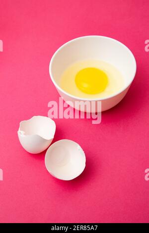 Broken egg in bowl near shell on pink surface Stock Photo