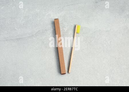 Ecological Bamboo toothbrushe with yellow nylon bristles and brown paper box on stone background. Concept of choosing natural products. Flat lay Stock Photo