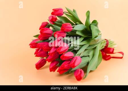 A large bouquet of red tulips with a red ribbon lies on a delicate beige background - spring flowers for the holiday of March 8 or Valentines Day. A p Stock Photo