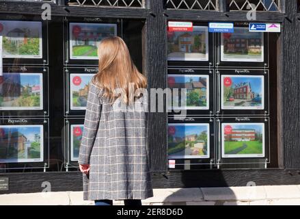 A young woman ( model released ) looking in an estate agent window in Surrey, England, Uk. February 2021 Stock Photo