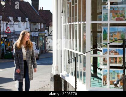 A young woman ( model released ) looking in an estate agent window in Westerham, Kent, England, Uk. February 2021 Stock Photo