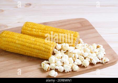 Boiled corn pob and sweet popcorn. Ears of cooked sweet corn on a wooden table scattered popcorn. Stock Photo