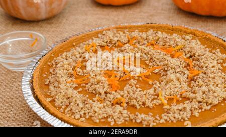 Fresh baked homemade pumpkin pie decorated with crushed nuts and orange zest close up in disposable baking pan, just from the oven Stock Photo
