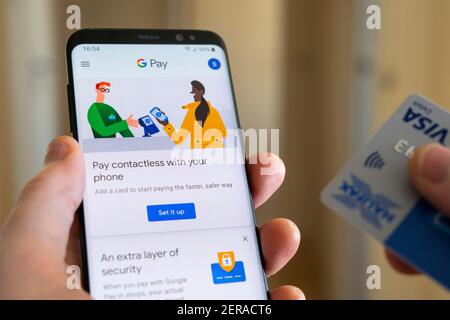 A man holding a debit card and smartphone with the Google Pay app to allow contactless payment by mobile phone Stock Photo