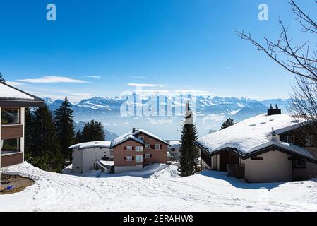 Unique panoramic alpine skyline view of Rigi resort. Snowed Chalets, wooden lodging cabins, hotels, iced Swiss Alps, blue sky. Mount Rigi, Weggis, Luc Stock Photo
