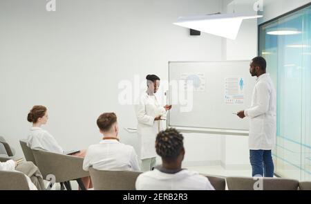Side view portrait of young African-American woman standing by whiteboard while giving presentation during medical seminar in college, copy space Stock Photo