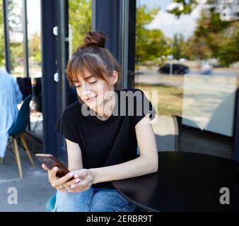 Charming woman hold mobile phone during rest in coffee shop. Happy Caucasian female relaxing in cafe during free time Stock Photo