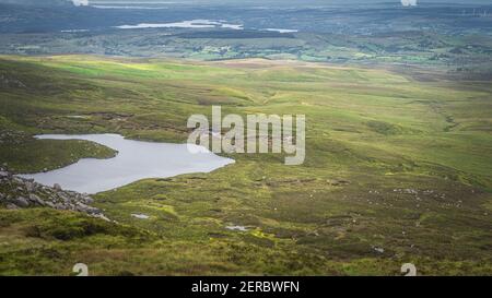 View from Cuilcagh Mountain on lakes, green meadows and fields with patches of sunlight in the valley below, Northern Ireland Stock Photo