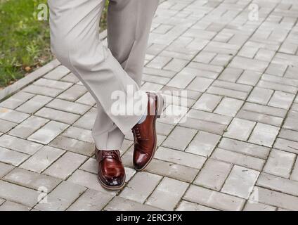 The man's legs are leg by foot in light trousers and brown shoes stand on paving tile. Stock Photo