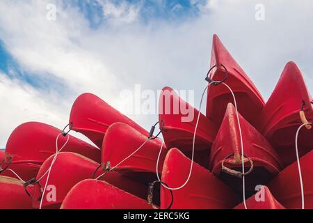 group of red kayaks piled up against each other on the shore seen from below with a blue sky in the background Stock Photo