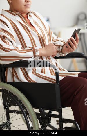 Cropped vertical portrait of modern handicapped woman using smartphone while sitting in wheelchair Stock Photo