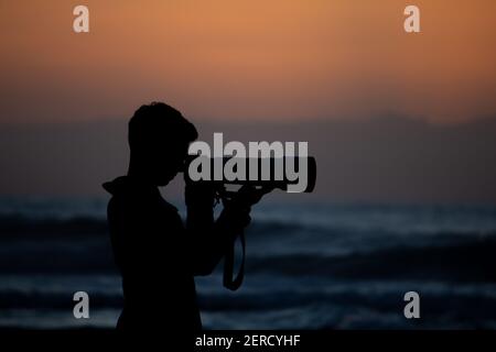 Amazing shilouette of a photographer taking a picture at the beach during sunset Stock Photo