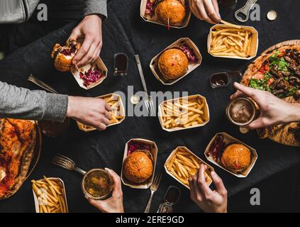 Lockdown family fast food dinner from delivery service. Flat-lay of friends having quarantine home party with delivered burgers, fries, sandwiches, pi Stock Photo