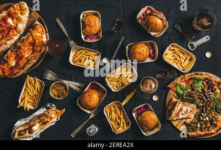 Lockdown takeaway fast food dinner from delivery service concept. Flat-lay of quarantine home party with burgers, french fries, sandwiches, pizza, bee Stock Photo