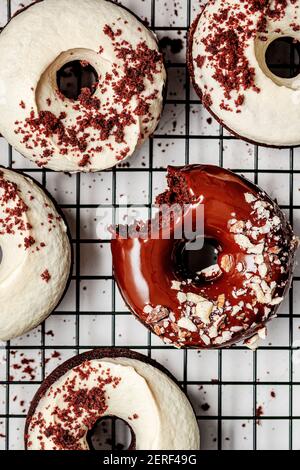 Baked chocolate donuts with chocolate glaze and cashew cream frosting, sprinkled with almonds and crumbs and served on a rack tray. Stock Photo