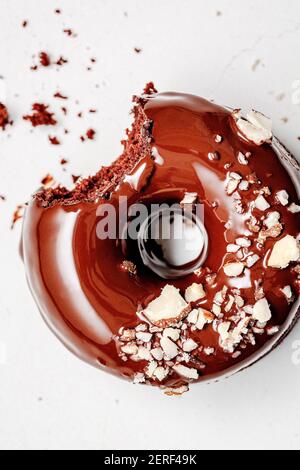 Bitten baked chocolate donut with chocolate glaze and almonds, on a white background with crumbs. Stock Photo