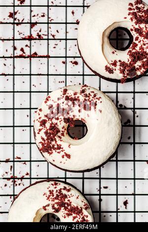 Three baked chocolate donuts with cashew cream frosting sprinkled with crumbs and served on a rack tray. Stock Photo