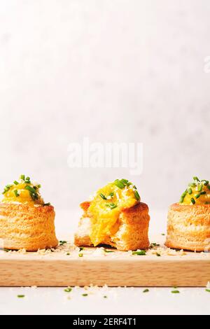 Three Vol-au-Vent filled with cauliflower and saffron sauce, lined on a wooden cutting board and sprinkled with cheese and chive. Stock Photo