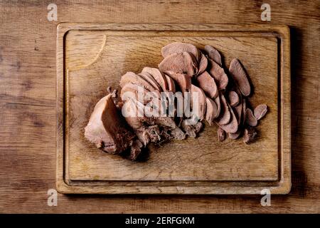 Baked beef tongue sliced, serving on wooden cutting board over wood background. Flat lay. Stock Photo