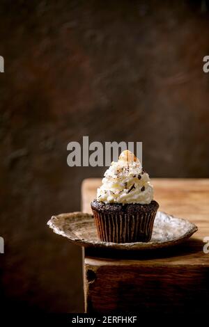 Homemade chocolate cupcakes muffins with white whipped butter cream and salted caramel on ceramic plate, served with chopped dark chocolate on wooden Stock Photo