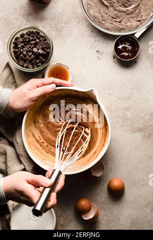 Hands mixing a bowl of brownie batter next to bowls of flour and chocolate chips. Stock Photo