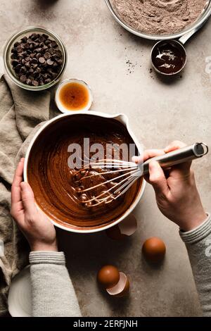 Hands mixing a bowl of brownie batter next to bowls of flour and chocolate chips. Stock Photo