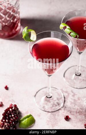 Two pomegranate cosmopolitans in martini glasses wiith a lime twists and a cocktail shaker. Stock Photo
