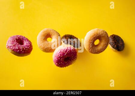Various decorated doughnuts in motion falling on yelloy background. Sweet and colourful doughnuts falling or flying in motion. Stock Photo