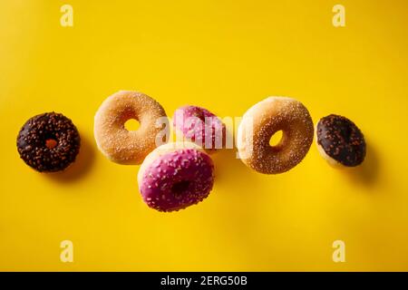 Various decorated doughnuts in motion falling on yelloy background. Sweet and colourful doughnuts falling or flying in motion. Stock Photo