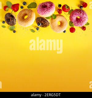 Various decorated doughnuts with sprinkles and berries in motion falling on yelloy background. Sweet and colourful doughnuts falling or flying in moti Stock Photo