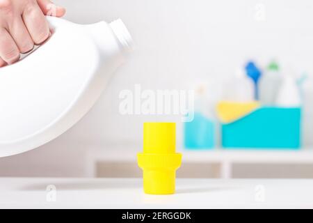 White chlorine bottle with yellow cover mock-up. Toxic detergent. Cleaning supplies in background. Using of measuring cup. Stock Photo