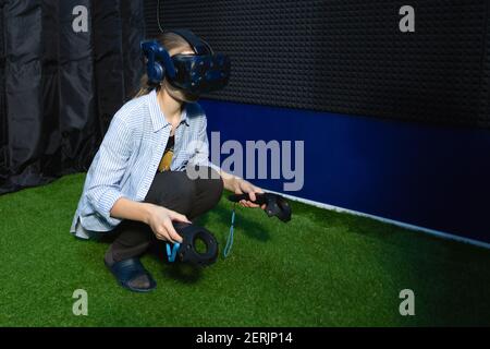Young teen girl wearing virtual reality goggles sitting on floor using controllers playing VR games in game club. Stock Photo