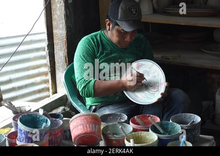 A man is seen painting pottery dishes in a small factory located