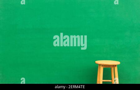 Single yellow wooden chair front of green wall background with copy space for text or design Stock Photo