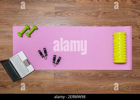 Fitness mat, dumbbells, expander and laptop for online workouts at home. Online learning concept in relation to the pandemic Stock Photo