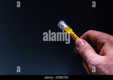 man holding a yellow network internet cable on a black background close-up with space for text Stock Photo