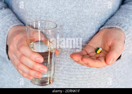 antibiotic pills, contraceptives and a glass of water in the hands of a young woman close-up Stock Photo