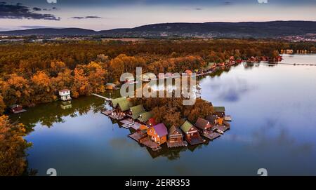 Tata, Hungary - Beautiful autumn sunset over wooden fishing cottages on a small island at Lake Derito (Derito-to) in October with clear blue sky and a Stock Photo