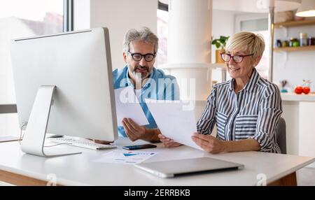 Happy mature business colleagues in modern office using computer and brainstorming. Stock Photo