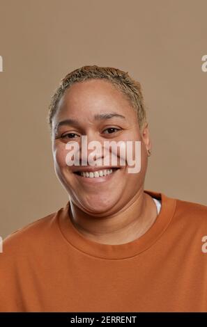 Vertical portrait of short haired mixed race woman looking at camera and smiling happily while posing against neutral background in studio Stock Photo