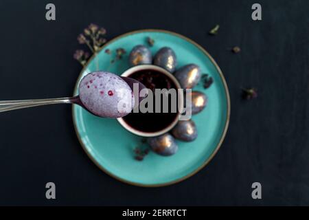 Easter concept of coloring eggs in hibiscus, eco diy. Top view, black background and turquoise plate. Egg in spoon on foreground. Stock Photo