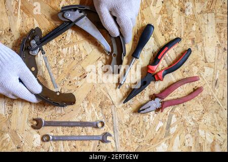 car drum brake disassembled in men's gloved hands and a set of various repair hand tools or auto mechanic's tools kit on a sheet of osb plywood backgr Stock Photo
