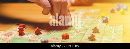 Russia, December 2020: two men friends have fun playing the carcassonne board game late in the evening or at night. male hands and game cards and chip Stock Photo