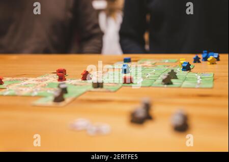Russia, December 2020: two men friends have fun playing the carcassonne board game late in the evening or at night. male hands and game cards and chip Stock Photo